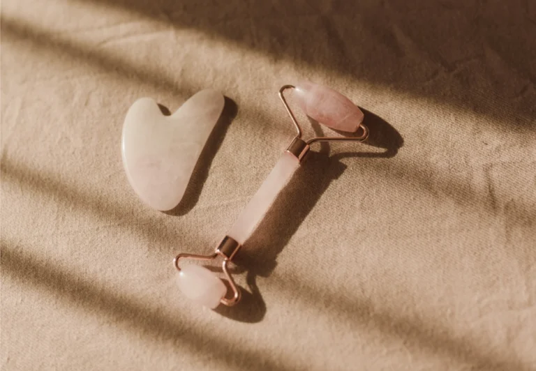 Aesthetic stock image shows a jade face roller and Gua Sha tool on a bed with beige sheets. The image is purely for decorative use only to support the wellness daily blog post