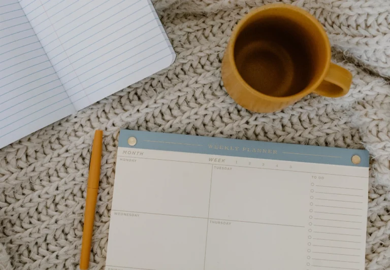 Aesthetic stock image showing a weekly planner open on a bed with another open notebook and cup of coffee. The image is purely for decorative us only to support the blog post on the burnout recovery plan I swear by.