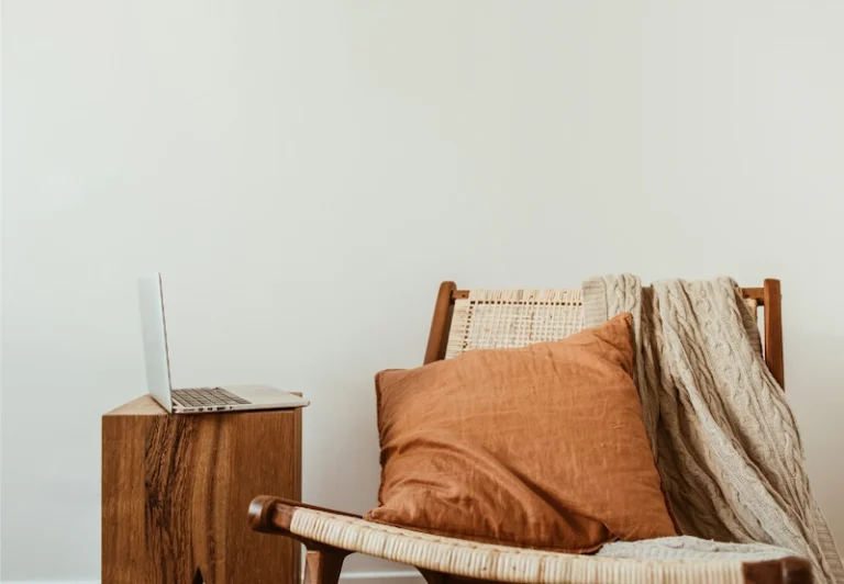 Aesthetic stock image showing a wicker chair with an orange cushion next to a wooden coffee table with an open laptop. The image is purely for decorative us only to support the blog post on career change.