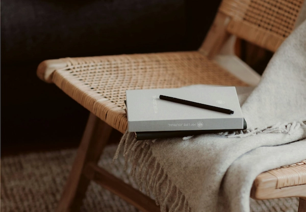 Aesthetic stock image showing a notebook lying on a blanket on a wicker chair next to a pair of cosy slippers. The image is purely for decorative use only to support the blog post on journal prompts to find your dream career