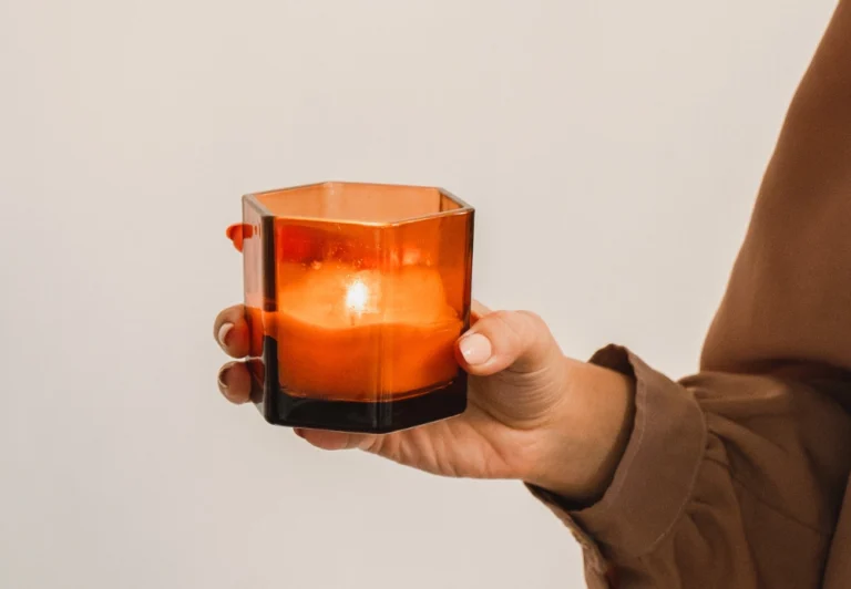 Aesthetic stock image showing a woman holding a lit candle in an orange holder. The image is purely for decorative use only to support the blog post on relaxing evening rituals for a better night's sleep