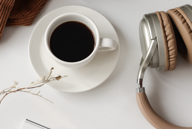 Aesthetic stock image showing a cup of coffee on a white table with a pair of brown headphones. The image is purely for decorative us only to support the blog post on how to boost your mood on a rainy day.