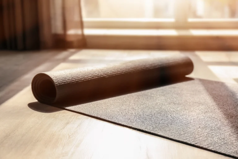Aesthetic stock image shows a half rolled up yoga mat on a wooden floor with the sun coming through. The image is purely for decorative use only to support the blog post on how to build healthy habits that actually serve you