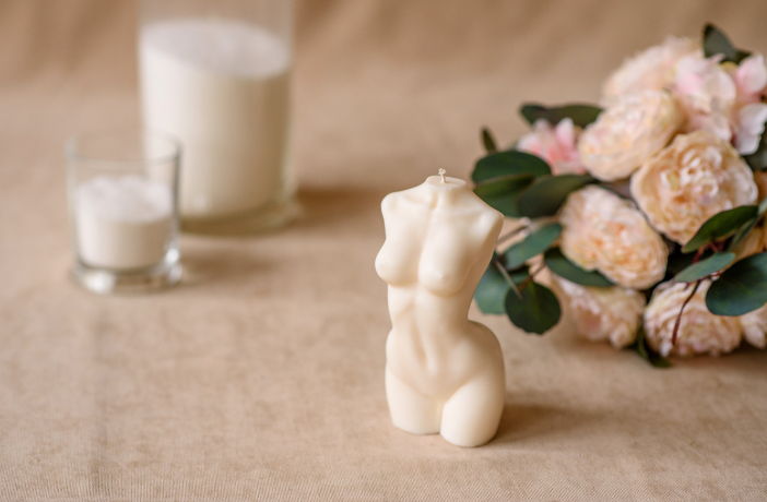 Aesthetic stock image showing a body-shaped wax candle on a marble table top next to a bouquet of pink roses. The image is purely for decorative use only to support the blog post on how to glow up mentally and physically in 2024