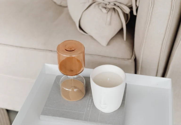 Aesthetic stock image showing a sand dial alongside a scented candle on a coffee table in front of a beige sofa. The image is purely for decorative us only to support the blog post on how to stop procrastinating.