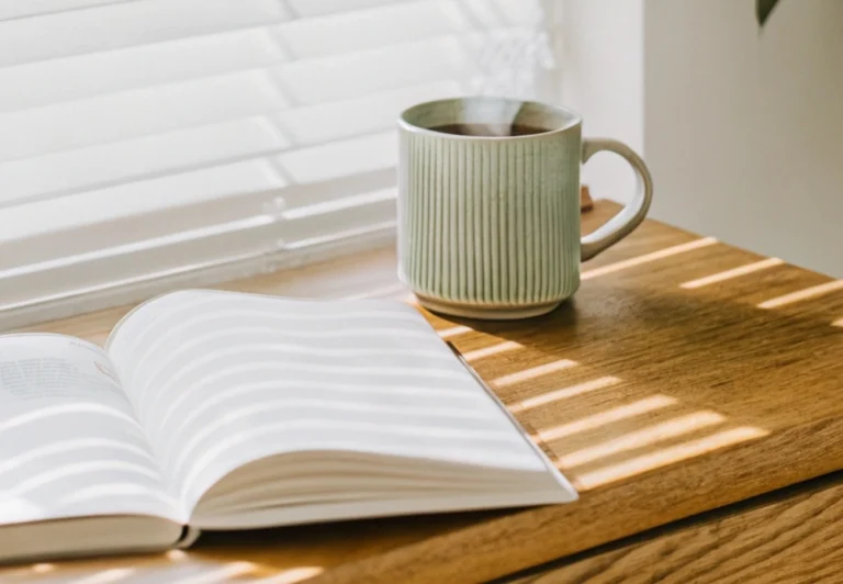 Aesthetic stock image showing an open journal on a window sill next to a mug of coffee. The image is purely for decorative us only to support the blog post on 51 journal prompts to reconnect with what lights you up.