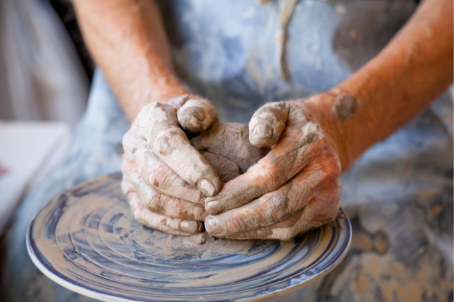 Stock image showing a woman making pottery with clay hands and wearing a blue apron covered in clay. The image is for decorative use only to support the blog post on meaningful hobbies for women in their 30s