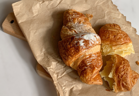 Aesthetic stock image showing a plain croissant on top of a brown paper takeaway bag. The image is purely for decorative use only to support the blog post on how to make your daily commute more enjoyable.