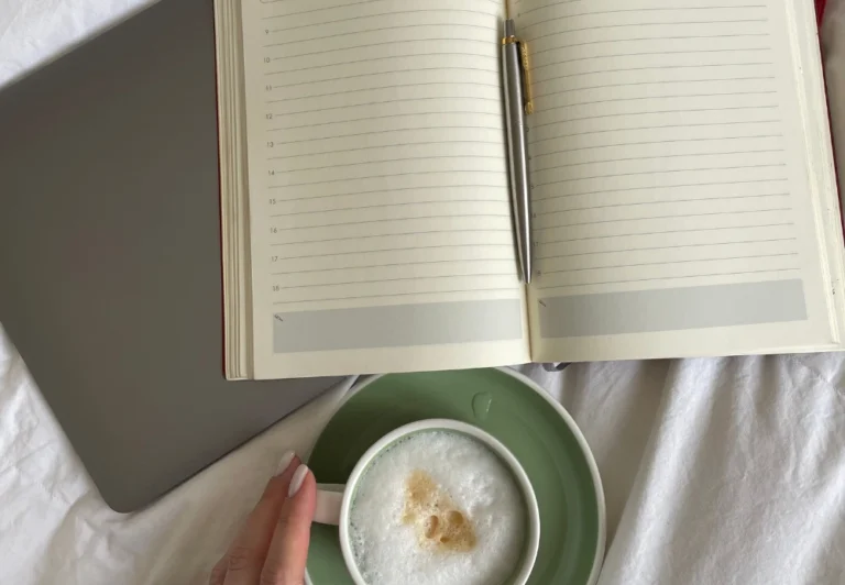 Aesthetic stock image showing an open lined journal on a bed with white sheets on top of a laptop. The image is purely for decorative use only to support the blog post on productive morning routine ideas.