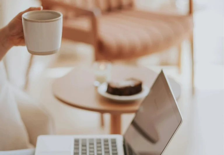 Aesthetic stock image showing a woman sat in front on a open laptop in her living room. The image is purely for decorative us only to support the blog post on whether you should tell your boss you’re burnt out.