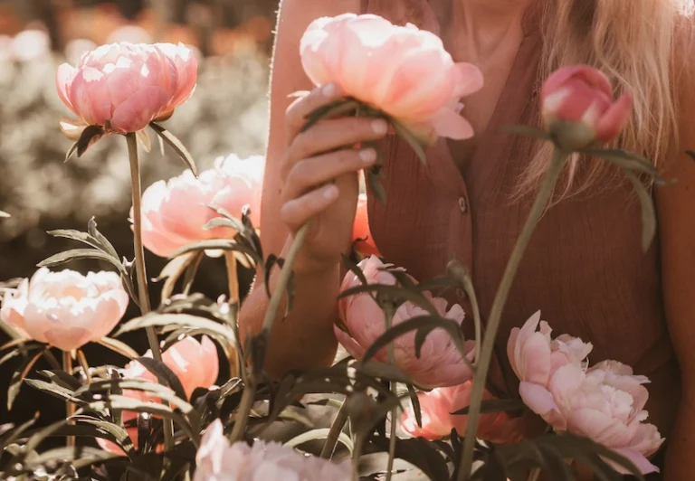 Aesthetic stock image showing a woman next to a rose bush smelling the flowers. The image is purely for decorative us only to support the blog post on the soft girl era.