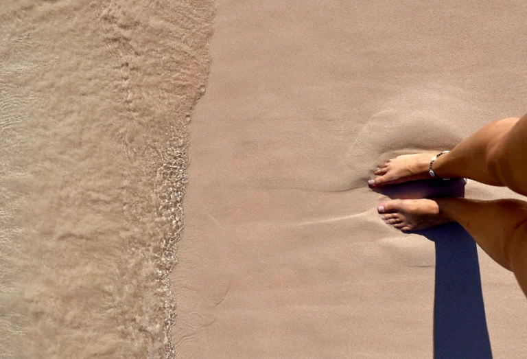 The author of Notes by Thalia, Thalia's feet are planted in pink sand on a beach in the Komodo Islands on Indonesia.