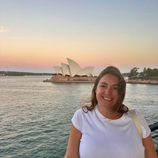 Lifestyle photo showing the author of Notes by Thalia, Thalia smiling at the camera during sunset in front of the Sydney opera house