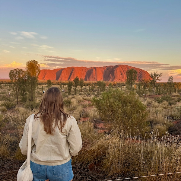 Lifestyle photo showing the author of Notes by Thalia, Thalia with her back towards the camera watching the sunrise above Ayers Rock in Uluru, Australia