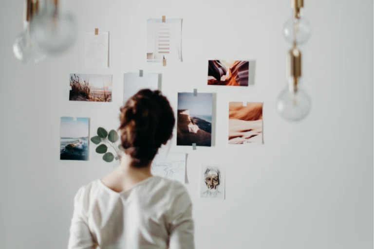 Aesthetic stock image showing a woman standing in front of a white wall with multiple different images taped to it. The image is purely for decorative use only to support the blog post on life goals to add to your vision board for 2025
