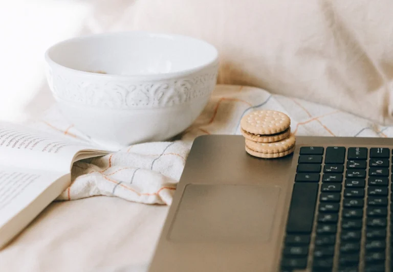 Aesthetic stock image showing an laptop open on a bed with an open notebook. The image is purely for decorative us only to support the blog post on what causes overstimulation.