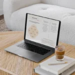 A laptop showing two pages from the Stay & Slay Workbook. The laptop is open on a brown coffee table